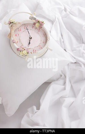 Metal clock on pillows on a big white bed Stock Photo