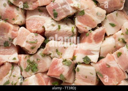 Raw, rindless, cubed British belly pork bought from a supermarket in the UK that has been marinated in lemon juice and fresh, chopped marjoram before Stock Photo