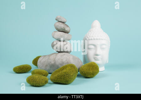 a pile of Zen stones in balance next to a Buddha's head surrounded by sparkling rocks on a turquoise summer background. Minimum color still life. Stock Photo