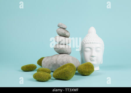 a pile of Zen stones in balance next to a Buddha's head surrounded by sparkling rocks on a turquoise summer background. Minimum color still life. Stock Photo