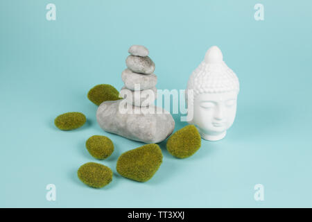 a pile of Zen stones in balance next to a Buddha's head surrounded by sparkling rocks on a turquoise summer background. Minimum color still life. Stock Photo