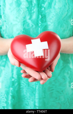 Red heart with cross sign in female hand, close-up, Stock Photo