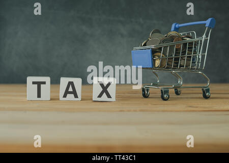 Buying and shopping online tax concept, tax on wooden with full money coins in cart on wooden table Stock Photo