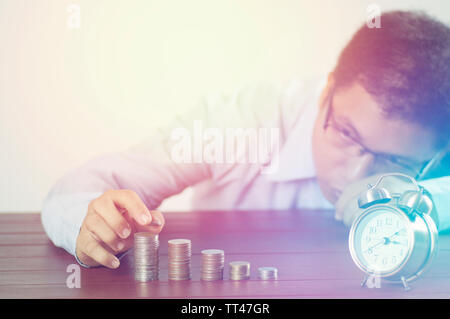 business man put money on pile of coins with alarm clock on working table, concept in time to success Stock Photo
