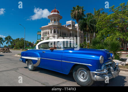 1950's American car drives past the Palacio de Valle, now a restaurant, on the Punta Gorda, Cienfuegos, Cuba Stock Photo