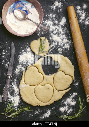 baking cheese cookies recipe photo of empty food background with cookies heart shape cut out of dough, rolling pin, flour, rosemary and vintage knife Stock Photo