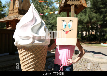 Woman with cardboard box on her head with happy face near big ice cream, outdoors Stock Photo