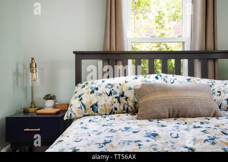 A comfortable room with a bed in front of a window on a sunny day and a nightstand with some objects on it. Stock Photo
