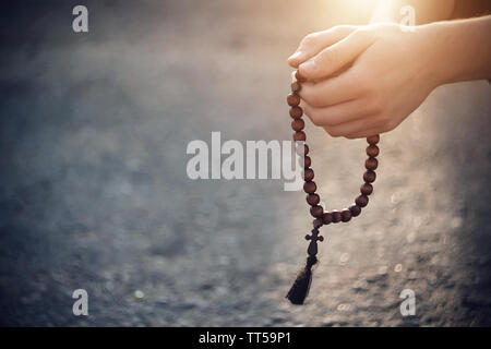 The Christian holds in his hands, folded in prayer, wooden rosaries, on which the light of heavenly illumination falls. Stock Photo