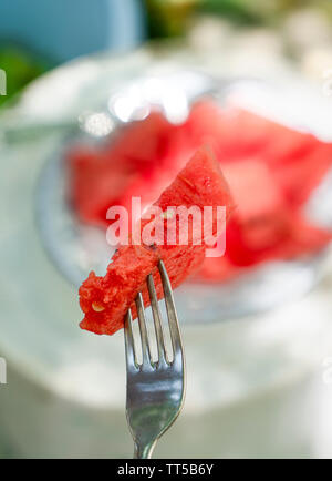 Slice of red watermelon on a fork and watermelon slices in bowl on background. Stock Photo