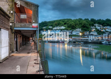 After another chilly overcast day the lights flicker on as the daylight gives way to dusk in the historic fishing port of Looe in Cornwall. Stock Photo
