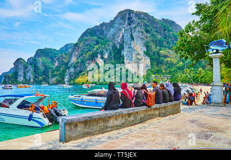PHIPHI DON, THAILAND - APRIL 27, 2019: The group of muslim tourists enjoys the seaside views, sitting at the pier on Tonsai Bay of Phi Phi Done Island Stock Photo