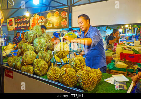 AO NANG, THAILAND - APRIL 27, 2019: The stall of Ao Nang Night Market with heap of durians, the merchant checks the fruits' ripeness, knocking their t Stock Photo
