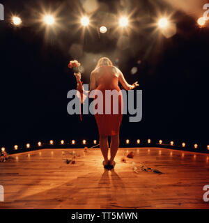 Woman on stage taking a bow holding  flowers wearing a red dress Stock Photo