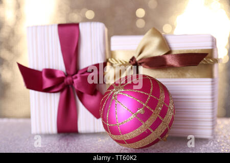 Gift boxes with vinous and golden ribbons and bows and Christmas tree toy on table on shiny background Stock Photo