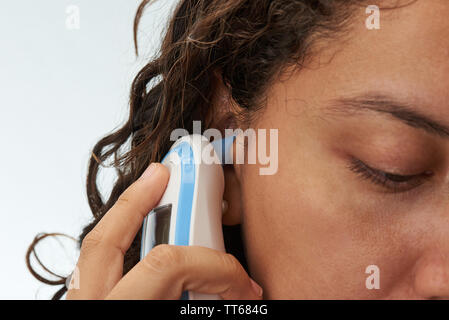 Close-up of digital body thermometer in woman ear Stock Photo