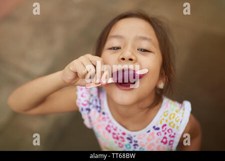 Small girl bites ice cream on wooden stick above top view Stock Photo