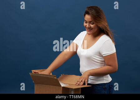 Young woman unboxing package isolated on blue studio background Stock Photo