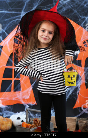 Little girl in hat with pail for candy on Halloween decorations background Stock Photo