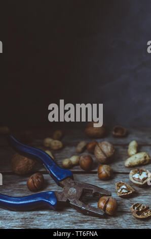 Various nuts, peanuts, hazelnuts and walnuts on old wooden table with tongs, tinted photo Stock Photo