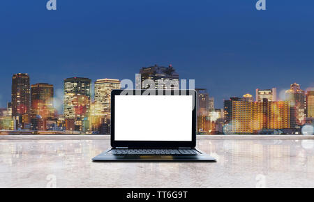 Computer laptop blank white screen on concrete with city view at night with Bokeh lights. Laptop Computer Background Stock Photo
