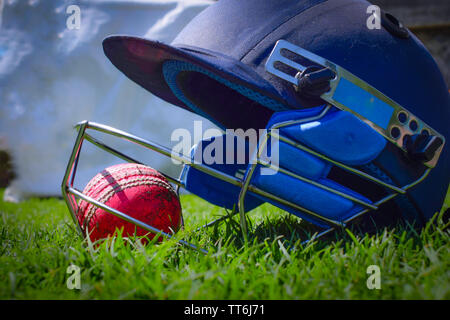 Cricket halmet and a ball on a green grass. Helmet protects batsman from fast balls which may otherwise cause harm to playing person. Stock Photo