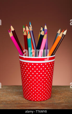 Colorful pencils in red plastic cup on wooden table and shaded color background Stock Photo