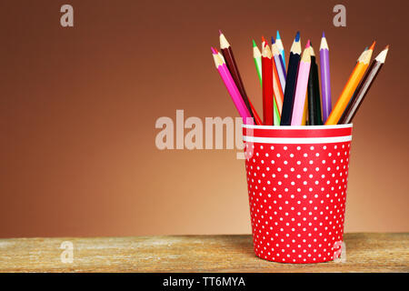 Colorful pencils in red plastic cup on wooden table and shaded color background Stock Photo