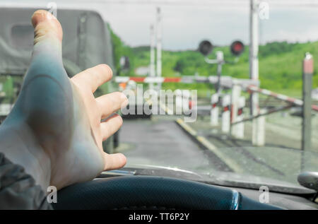 The hand of man inside the car. The car stopped in front of a closed barrier and a red traffic light before the railway crossing. Stock Photo