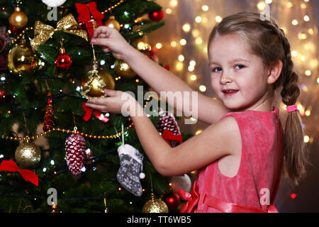 Little girl decorating Christmas tree on bright background Stock Photo