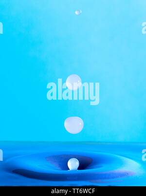 water drop falling and impacting a body of water after hitting the surface and forming different water droplets on a blue background. Stock Photo
