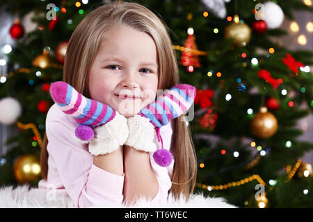 Little girl with mittens lying on fur carpet on Christmas tree background Stock Photo