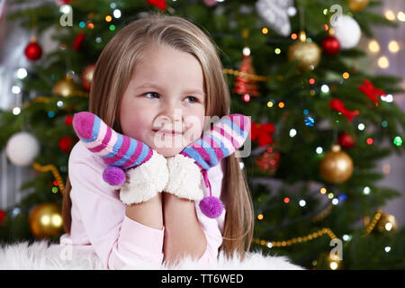 Little girl with mittens lying on fur carpet on Christmas tree background Stock Photo