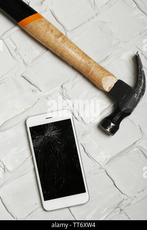 Broken iPhone with hammer on brick background Stock Photo
