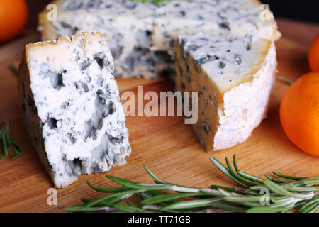Blue cheese with sprigs of rosemary and orange on wooden board background Stock Photo
