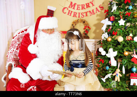 Little cute girl giving letter with wishes to Santa Claus near Christmas tree at home Stock Photo