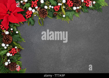 Poinsettia flower background border with silver ball baubles, holly, mistletoe and winter flora on grunge grey background with copy space. Traditional Stock Photo