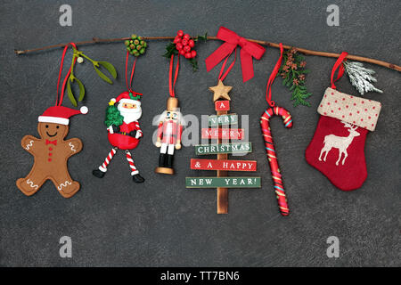 Christmas tree decorations hanging on a branch with winter flora and baubles of santa claus, candy cane, stocking,  nutcracker, tree and gingerbread c Stock Photo