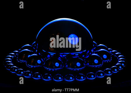 Steel balls in orbit around one another in a blue vivid hard light.  A very subtle steampunk scientist is reflected in the large steel ball in the cen Stock Photo