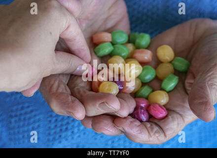 A young hand picks a hard candy from palm of a senior person Stock Photo