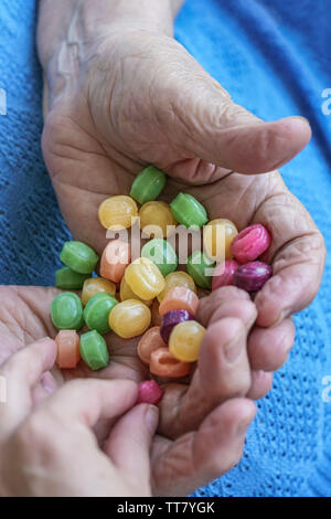 A young hand picks a hard candy from palm of a senior person Stock Photo