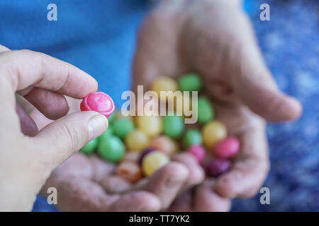 A young hand picks a hard candy from palm of a senior person Stock Photo