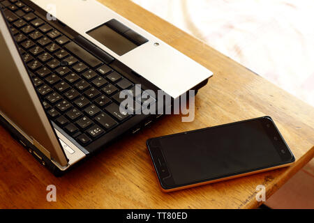 Photo of a laptop computer and smartphone on a table inside a bedroom Stock Photo