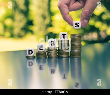 Symbol for increasing debts. Dice form the word "debts" on increasing high stacks of coins. Stock Photo