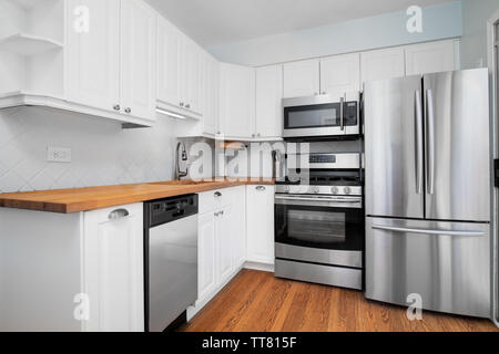A small kitchen with stainless steel appliances, white cabinets, and a natural light colored wood counter top. Stock Photo