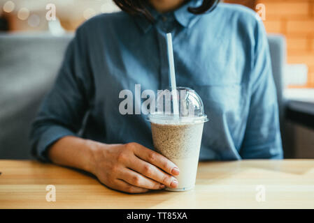 Girl in a blue shirt is holding a plastic cup with milkshake sitting in a restaurant Stock Photo