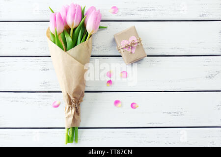 Beautiful pink tulips in paper with present box on wooden background Stock Photo
