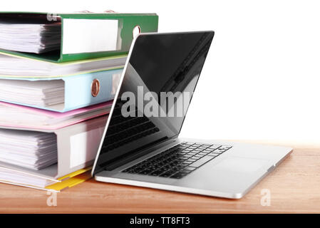 Laptop with stack of folders on table on white background Stock Photo