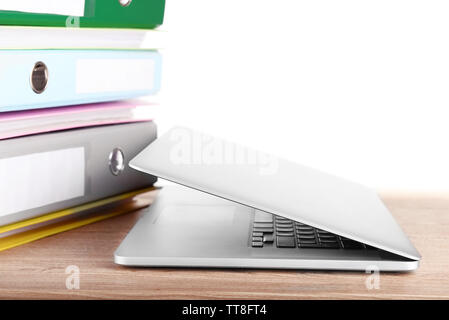 Laptop with stack of folders on table on white background Stock Photo
