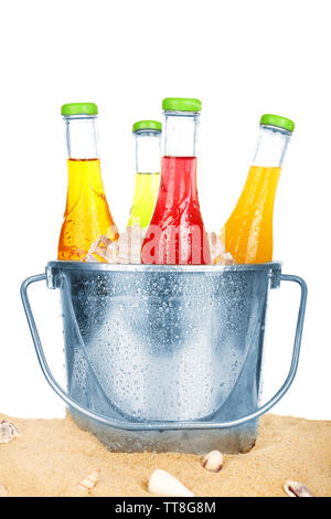 Bottles of tasty drink in metal bucket with ice on sand isolated on white Stock Photo
